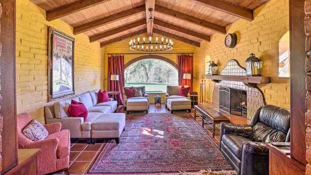 A cozy living room with a fireplace, wooden ceiling beams, and a large window.