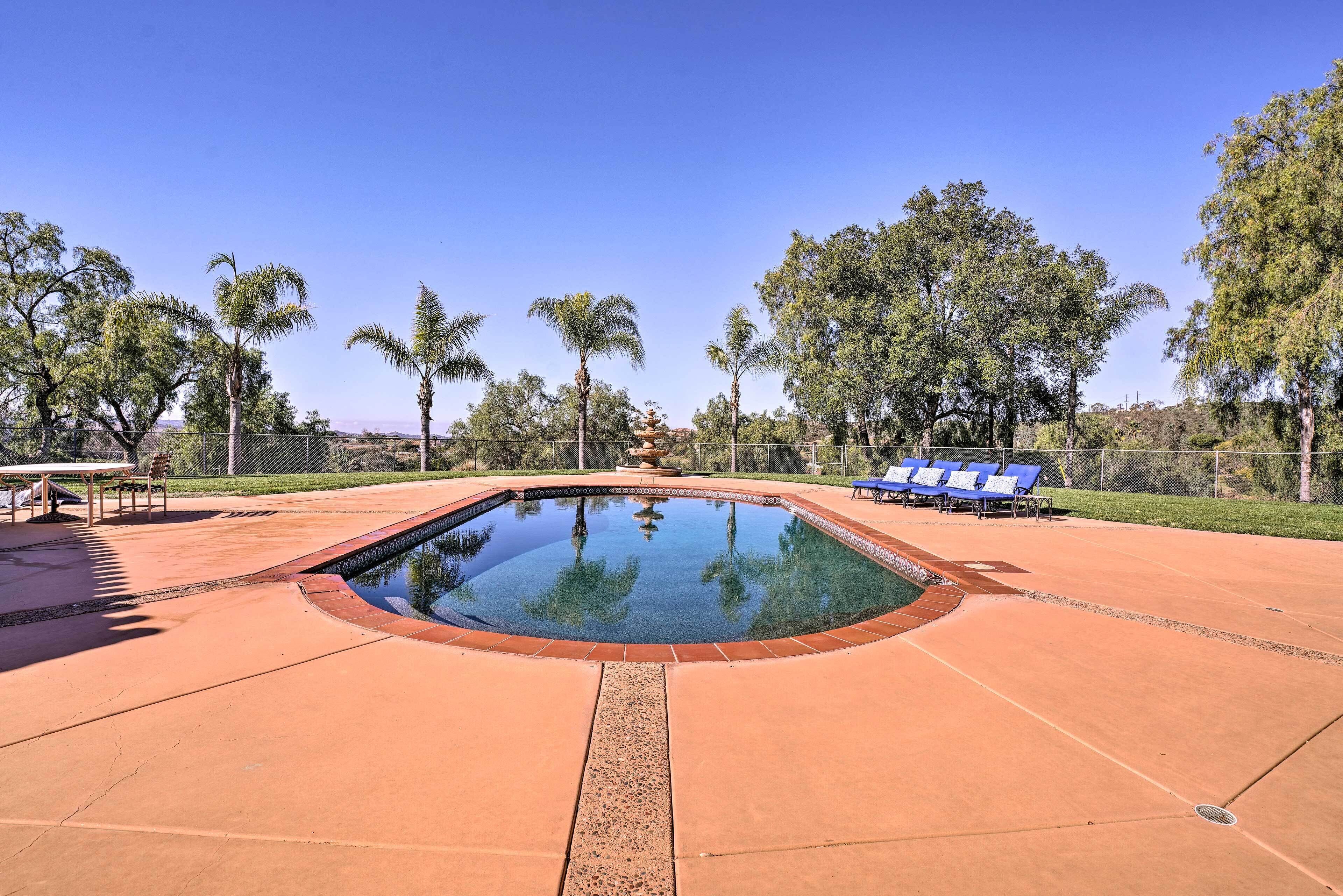 A swimming pool with a clear blue water surface, surrounded by a paved deck and palm trees.