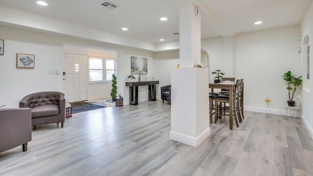 A spacious living room with a grey sofa, a dining table with chairs, and a kitchen area in the background. - Easy Intl Soccer Stay < 3 Mi to Hard Rock Stadium (Miami Gardens)