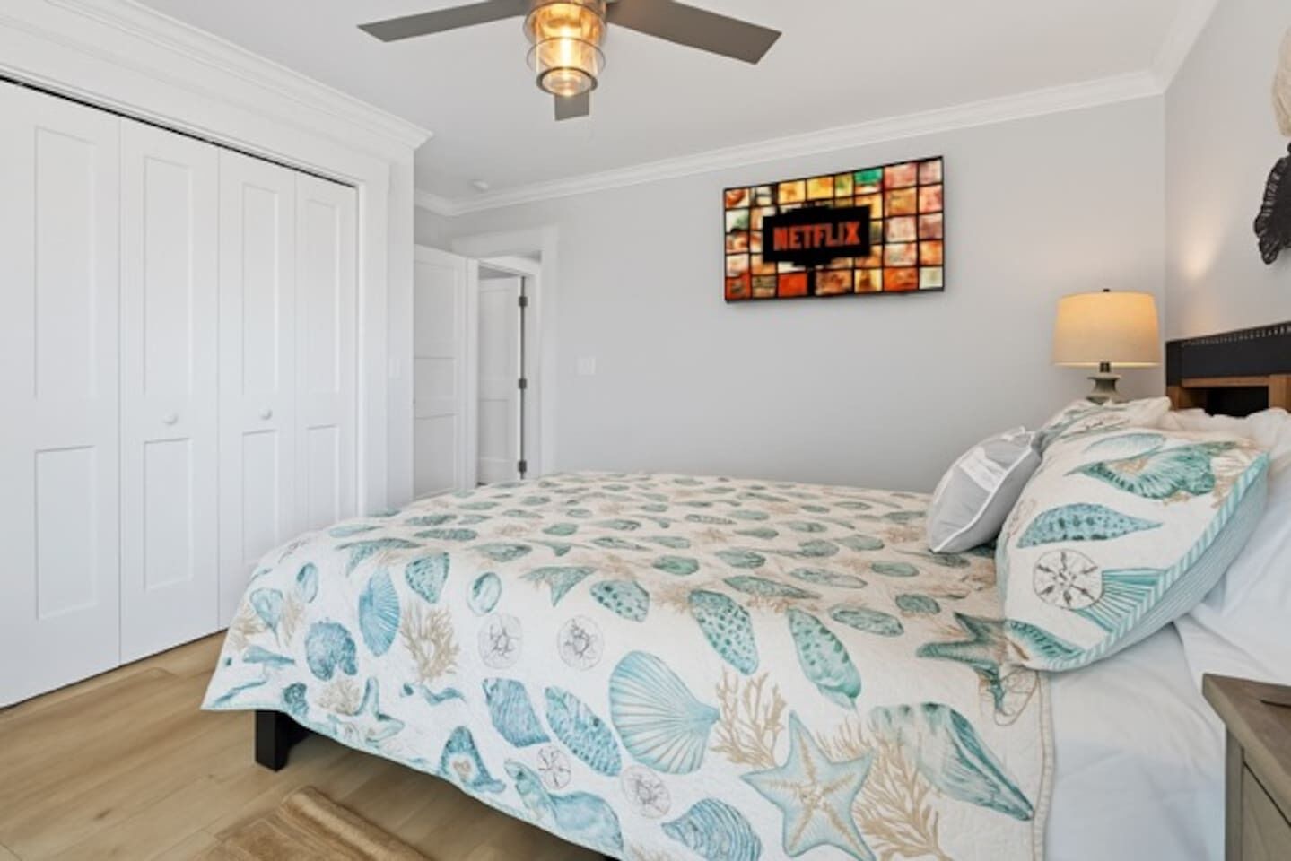 Ein Schlafzimmer mit einem Bett, einem Deckenventilator, einem an der Wand befestigten Fernseher und einer Tür.