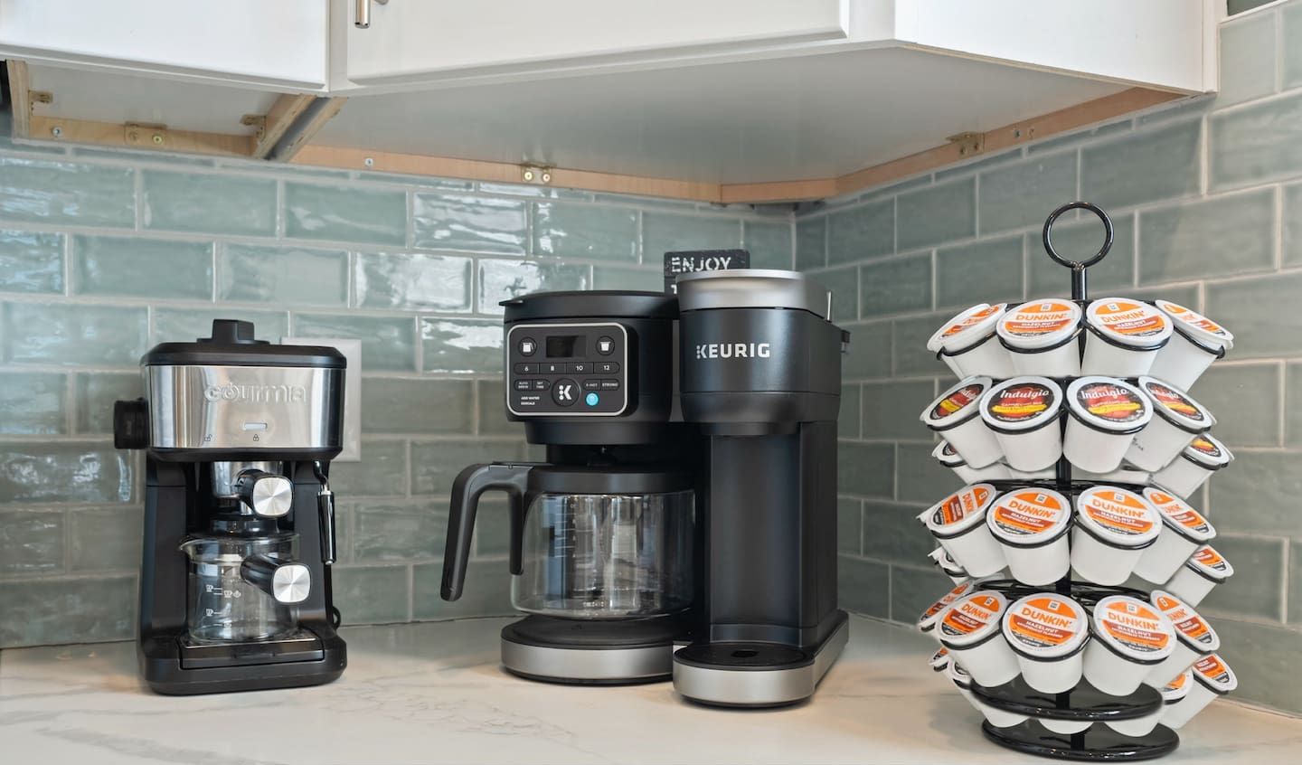 Een keuken met een koffiezetapparaat, een Keurig koffiemachine en een stapel Dunkin' Donuts bekers.