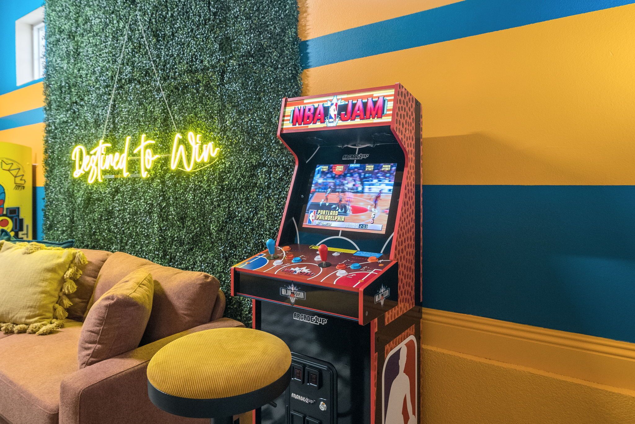 An arcade machine with a neon sign reading "NBA JAM" and a neon sign saying "Destined to Win" in the background.