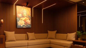 A modern living room with a sectional sofa, wooden paneling, and a large Buddha painting. - Hotel Maitreya Inn  (Vellore)
