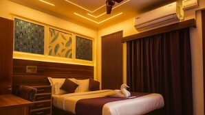 A hotel room with a large bed, a wooden headboard, a desk with drawers, and an air conditioning unit. - Hotel Maitreya Inn  (Vellore)