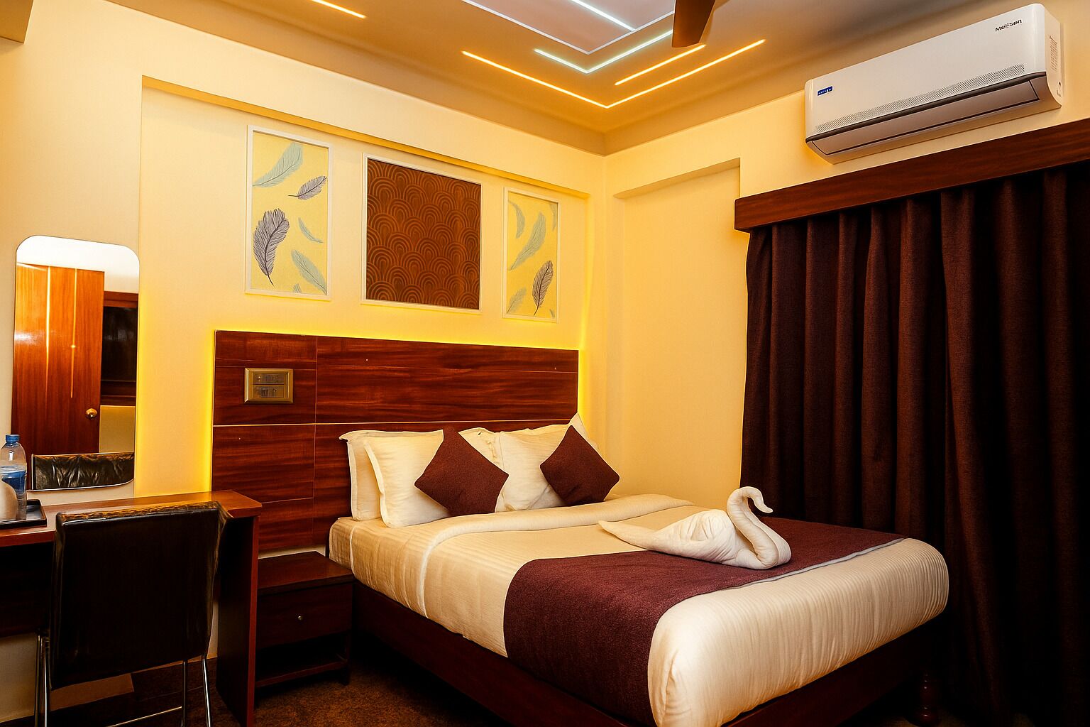 Habitación de hotel con cabecera de madera, cama con ropa de cama blanca y marrón, escritorio con silla, espejo y cuadros en la pared.
