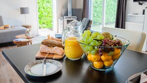 A breakfast table with bread, a pitcher of orange juice, and a bowl of fruit. - Luxury Holiday Chalet 1-4 persons with Private Jacuzzi, Private Sauna and Sun Shower. (Sint Jansklooster)