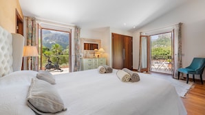 A spacious bedroom with a large bed, a dresser, a mirror, and a view of a mountain and patio. - Deluxe Villa Els Gorgs (Pollensa / Pollença)