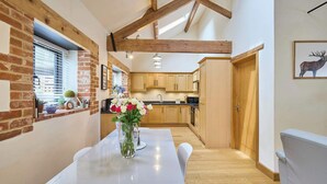A modern kitchen with wooden beams, a dining area with a white table, and a kitchen counter.