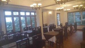 Comedor con varias mesas y sillas, amplias ventanas que dejan entrar luz natural y lujosos candelabros en el techo.