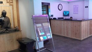 Un área de recepción con un mostrador de madera, una estatua de Buda, un reloj y una pantalla de televisión.
