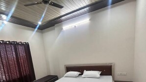 A bedroom with a single bed, a bench, a ceiling fan, and a window with curtains.