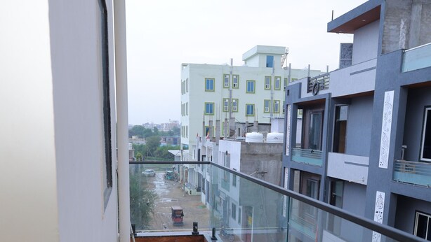 A narrow balcony with wooden flooring, glass railings, and a view of adjacent buildings.
