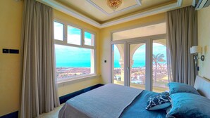A hotel room with a large bed, beige curtains, and a view of the city and ocean. - Villa Solara – Redefining Luxury Stays in Cyprus (Pegeia, Paphos, Cyprus)