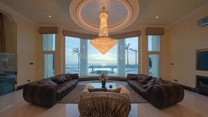 A spacious living room with a large chandelier, two sofas, a coffee table, and a view of the ocean through large windows. - Villa Solara – Redefining Luxury Stays in Cyprus (Pegeia, Paphos, Cyprus)