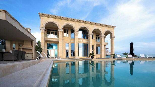 A poolside area with a clear view of a building featuring arched windows and a pool. - Villa Solara – Redefining Luxury Stays in Cyprus (Pegeia, Paphos, Cyprus)