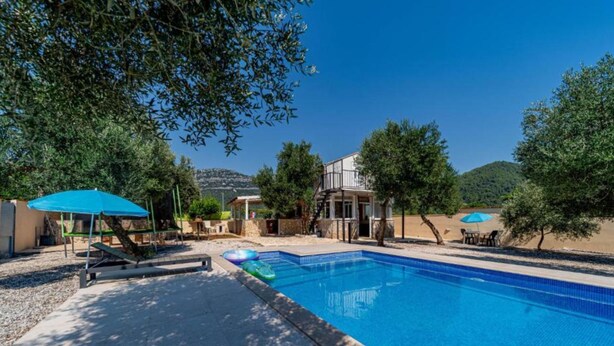 Une piscine à l’eau d’un bleu cristallin, entourée d’arbres et bordée d’un bâtiment doté d’un balcon.