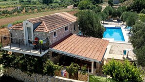 Une villa dotée d’une piscine, de murs en pierre et d’un balcon offrant une vue panoramique sur le paysage.