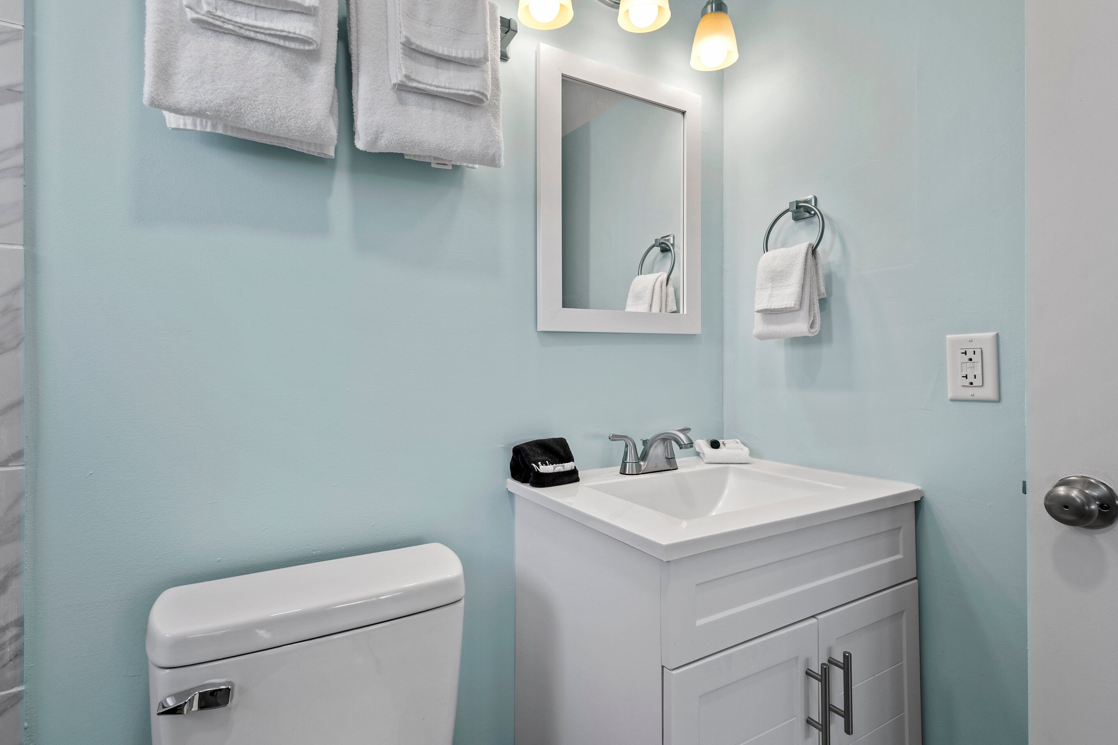 A bathroom with a white toilet, a white sink with a mirror above it, and a towel rack with folded towels.