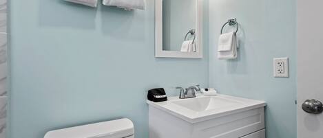 A bathroom with a white toilet, a white sink with a mirror above it, and a towel rack with folded towels.