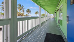 A covered walkway with a wooden floor and white railings, leading to a building with a blue exterior and a number '9' sign. - Oceanfront Inn Room #9 - Inlet View - King Bed (Fort Pierce)
