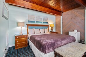 A bedroom with a bed, wooden headboard, two bedside tables with lamps, a dresser, and a patterned rug. - Oceanfront Inn Room #9 - Inlet View - King Bed (Fort Pierce)