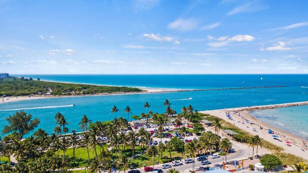 Un complejo turístico frente al mar con playa, zona de estacionamiento y abundante vegetación.
