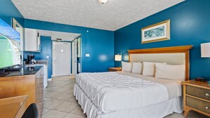 A hotel room with a large bed, a desk with a computer, a kitchenette, and a bathroom. - Oceanfront Inn Room #19- Ocean View Balcony, King Bed (Fort Pierce)