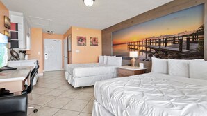 Une chambre d’hôtel avec deux lits, un bureau et un tableau représentant un coucher de soleil sur une jetée.