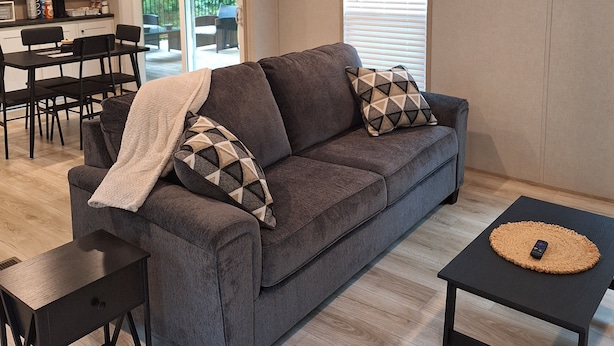 Ein modernes Wohnzimmer mit grauem Sofa, einem Couchtisch und einem Essbereich mit Tisch und Stühlen.