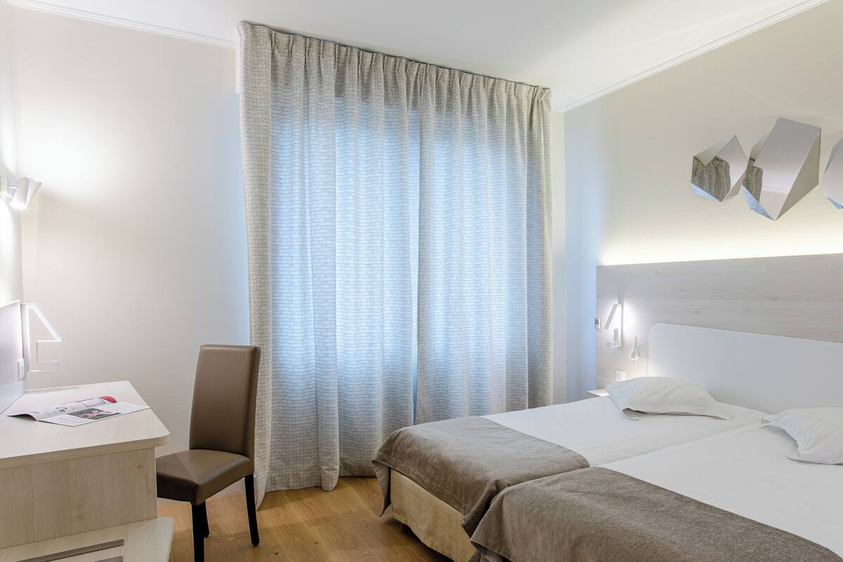 Une chambre d’hôtel avec un lit, un bureau, une chaise et une fenêtre avec des rideaux.