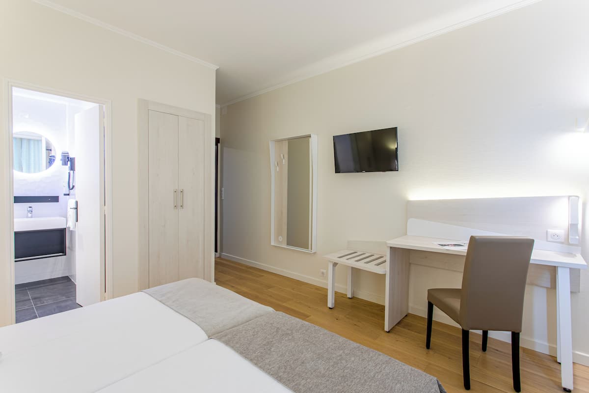 Une chambre d’hôtel avec un lit, un bureau, une chaise, une télévision et un miroir.