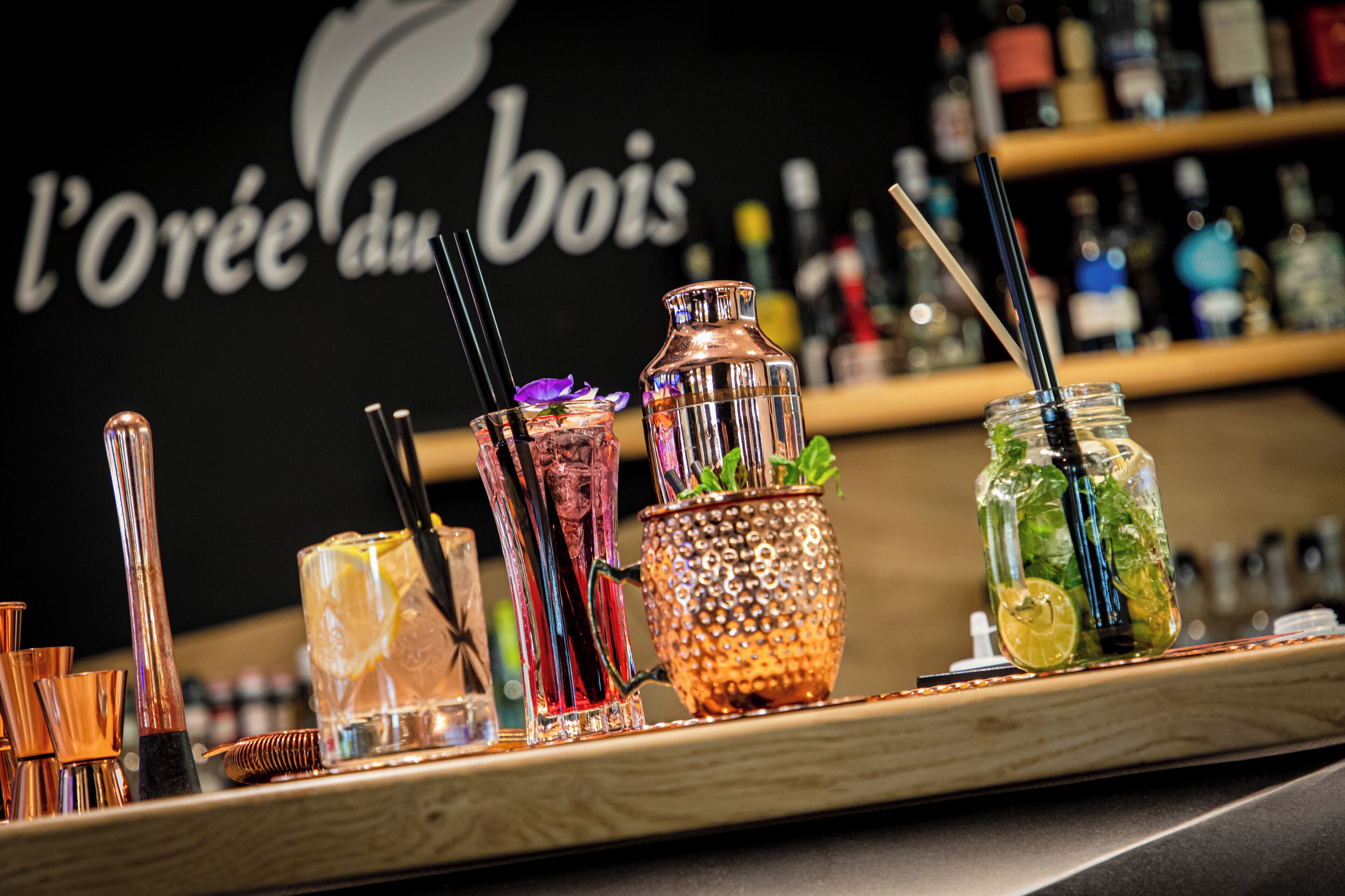 A bar area with various cocktail glasses and bottles, a copper-colored shaker, and a sign in the background.