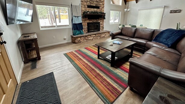 A spacious living room with a stone fireplace, leather sofa, and large windows offering views of the outdoors. - Modern and Cozy Cabin w Game Room,  Fireplace and all the amenities in PineTop (Pinetop Country Club)