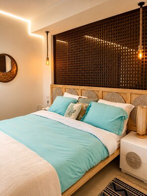 Ein ordentlich bezogenes Bett mit Holz-Kopfteil, ein Nachttisch mit Lampe und eine dekorative Wandverkleidung.