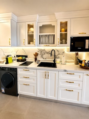 A modern kitchen with white cabinetry, a Bosch microwave, a washing machine, and a marble backsplash.