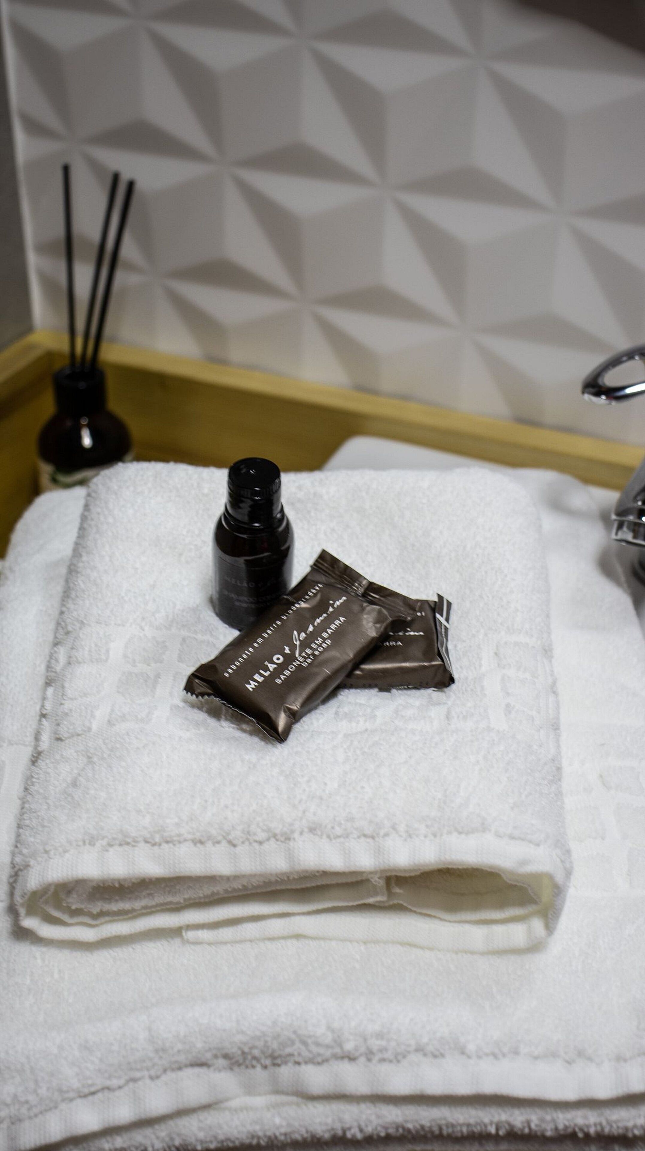 Une salle de bain avec une serviette blanche, une bouteille et deux paquets posés sur le lavabo.
