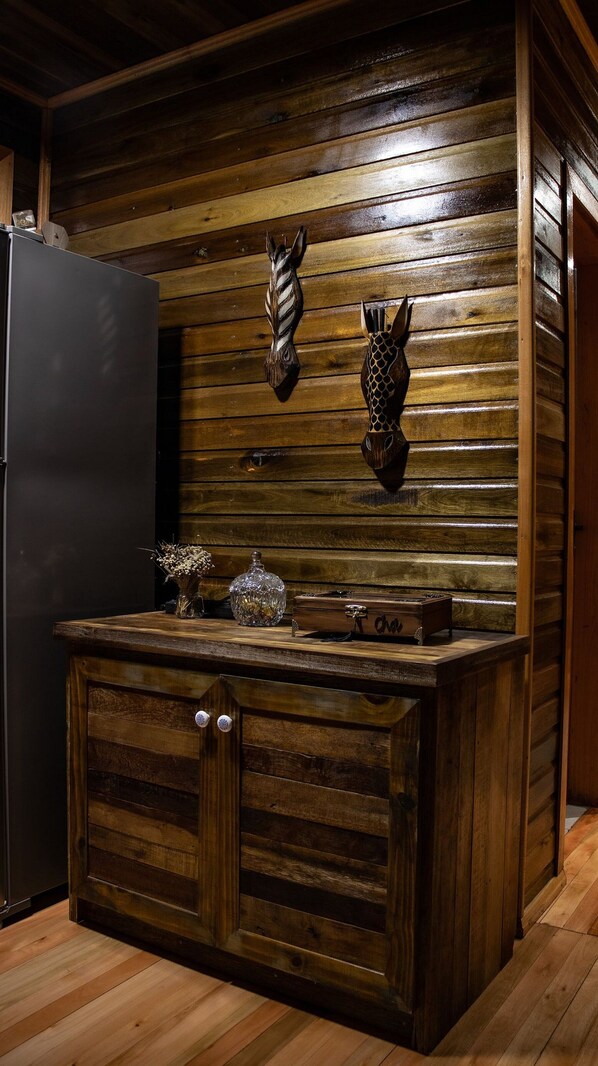 A kitchen with wooden paneling, a black refrigerator, a wooden cabinet with a lock, a vase with dried flowers, and two decorative masks on the wall. - Experiência Romântica no Cânion (Rio Fortuna)
