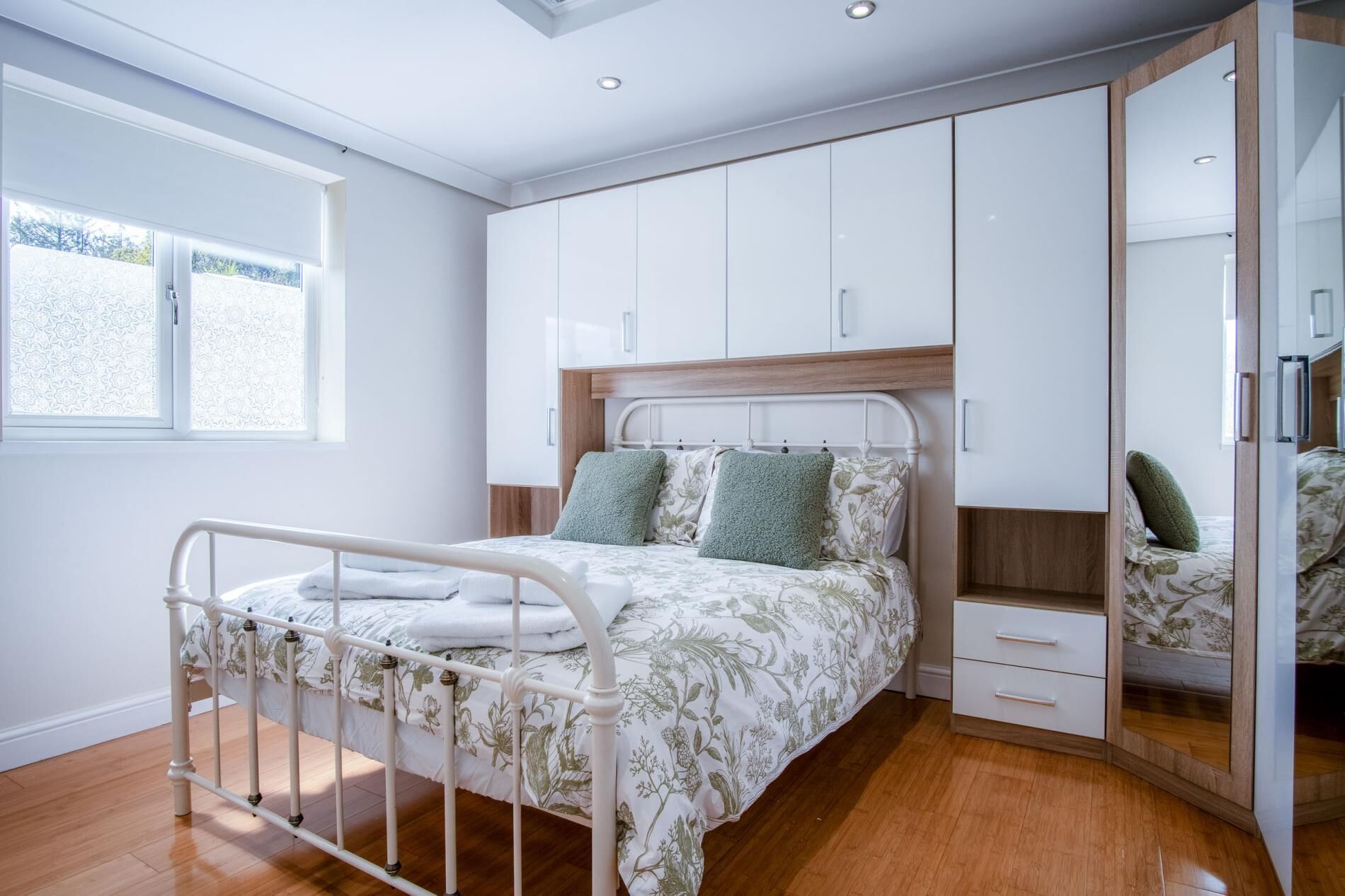 A bedroom with a bed, bedside drawers, a wardrobe, a mirror, and a window.