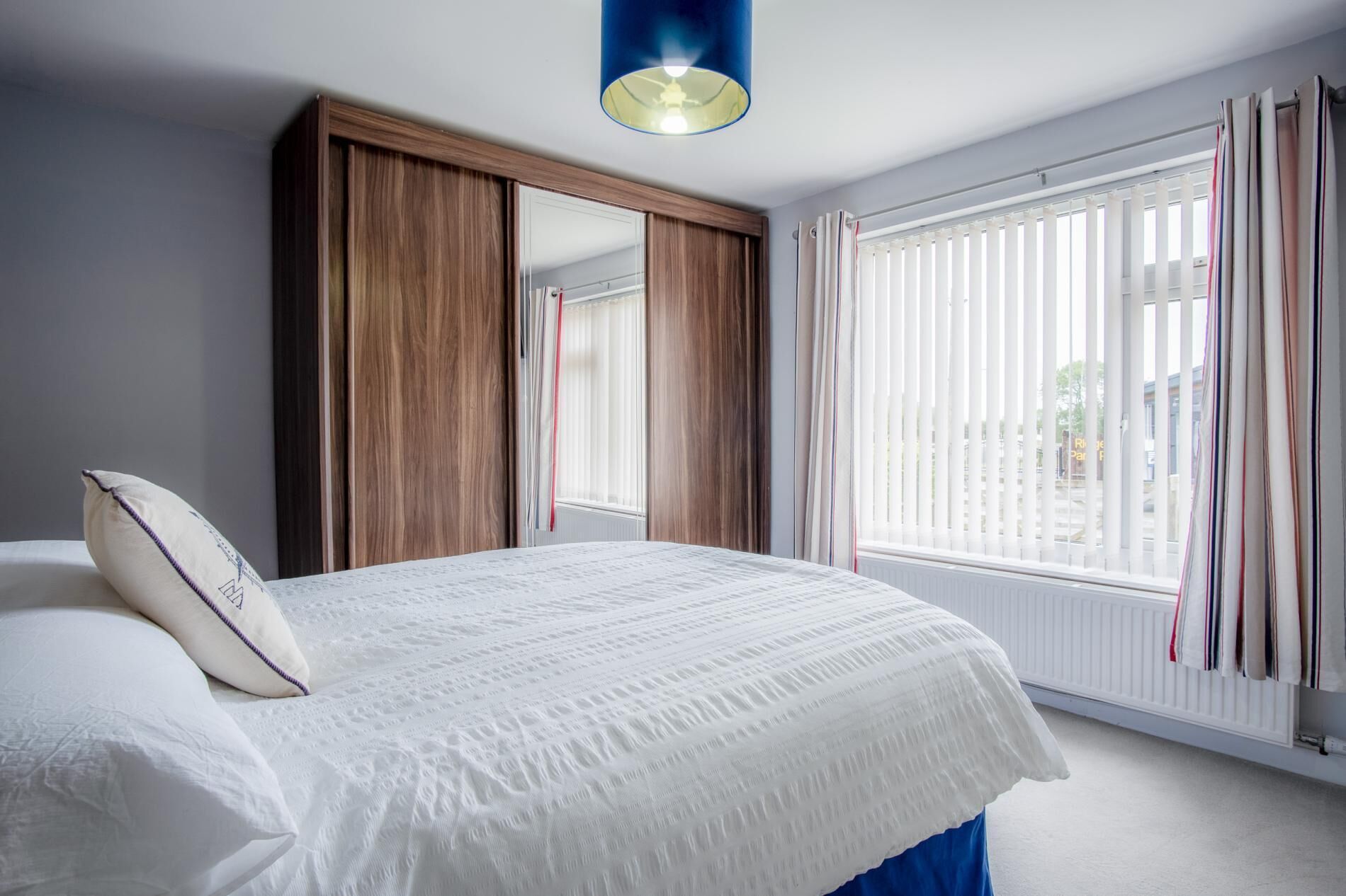 Un dormitorio con cama, un armario, una ventana con persianas y una lámpara colgante.