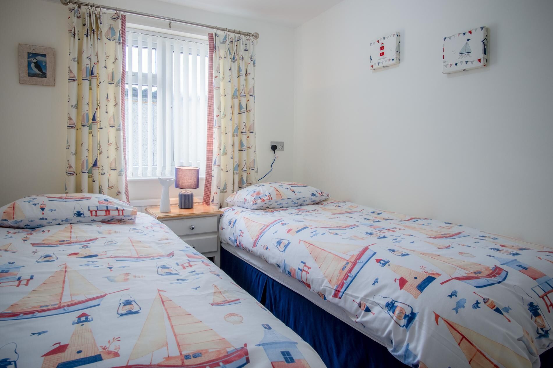 Un dormitorio con dos camas, una ventana con cortinas, una mesita de noche con lámpara y un reloj de pared.