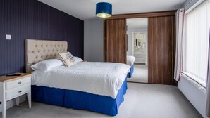 A bedroom with a tufted headboard, a bed with white and blue bedding, a nightstand, a blue hanging lamp, and a view of a bathroom through a sliding door.