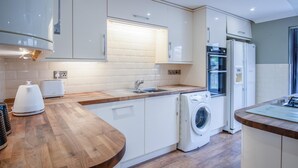 A modern kitchen with white cabinets, a wooden countertop, a built-in oven, a washing machine, and a sink.