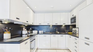 A modern kitchen with white cabinets, a black countertop, and a built-in oven. - 29 Rhodewood House - 2 Bedroom - Saundersfoot (Saundersfoot)