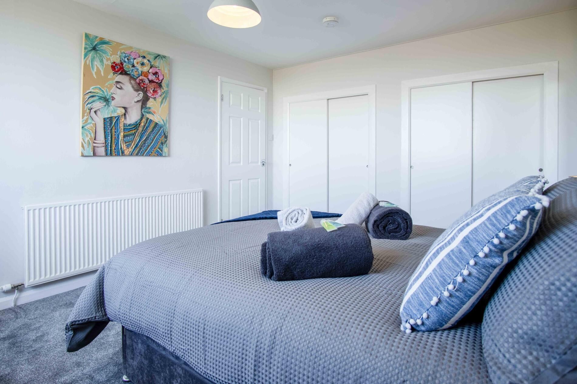 A bedroom with a bed, a painting, and a radiator.