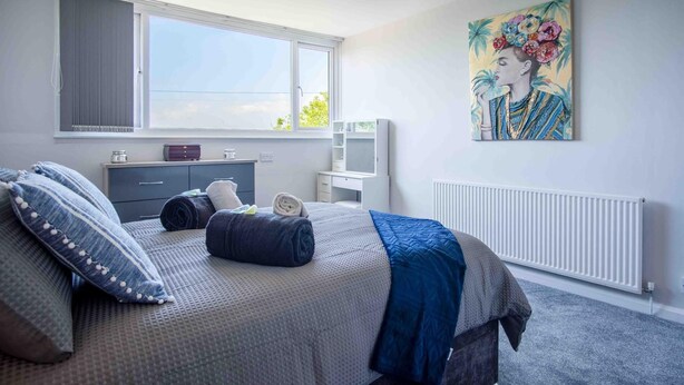 A bedroom with a bed, a dresser, a desk, a radiator, and a large window.