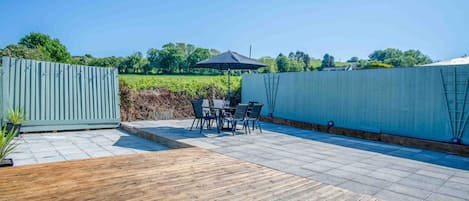 Eine Terrasse mit Holzdeck, einem Tisch und Stühlen sowie einem schwarzen Sonnenschirm.