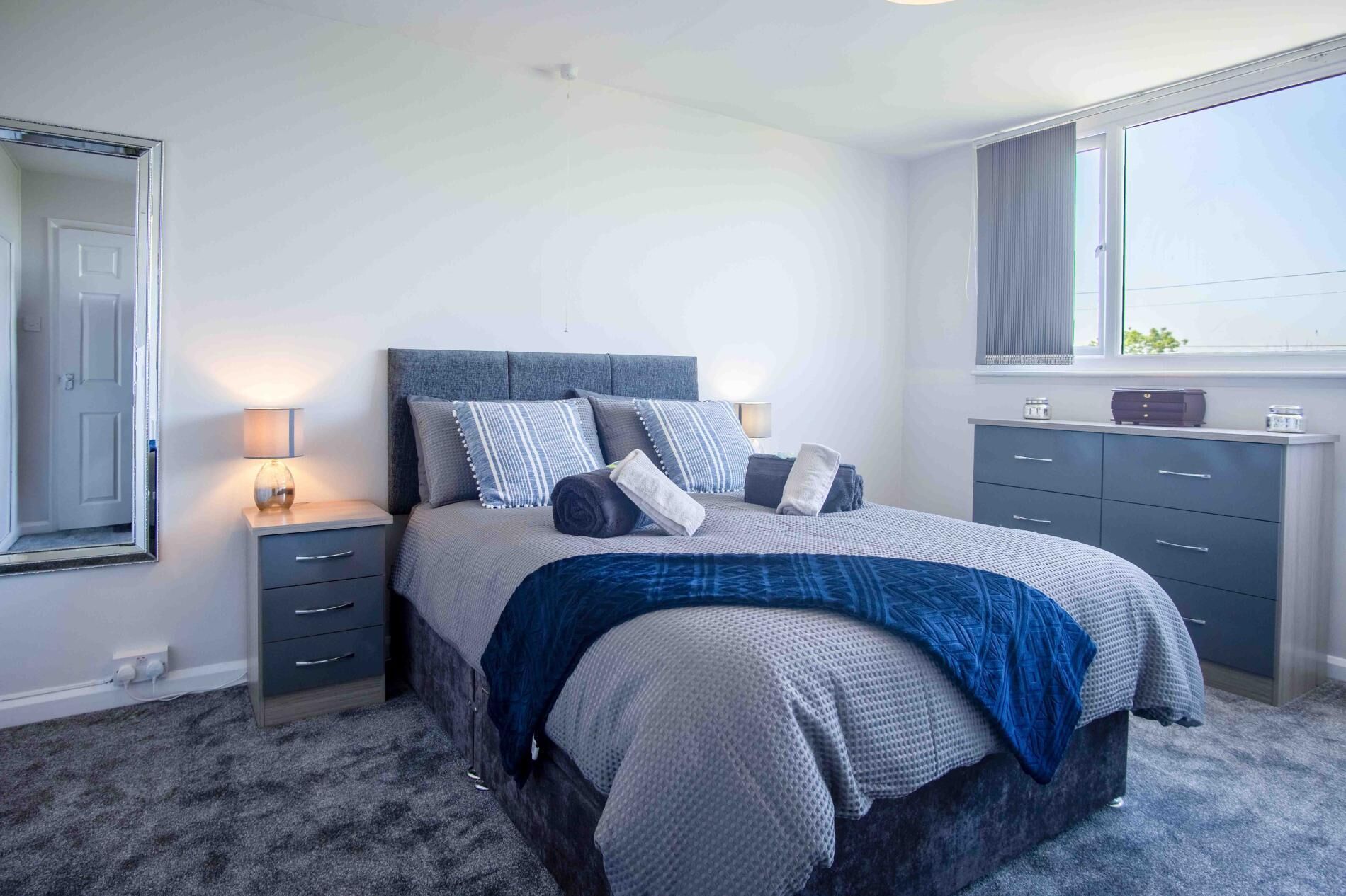 A bedroom with a bed, bedside tables, a dresser, and a window.