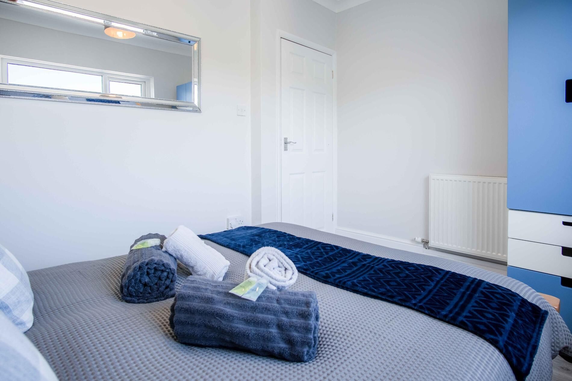 A bedroom with a bed, a mirror, a door, and a radiator.