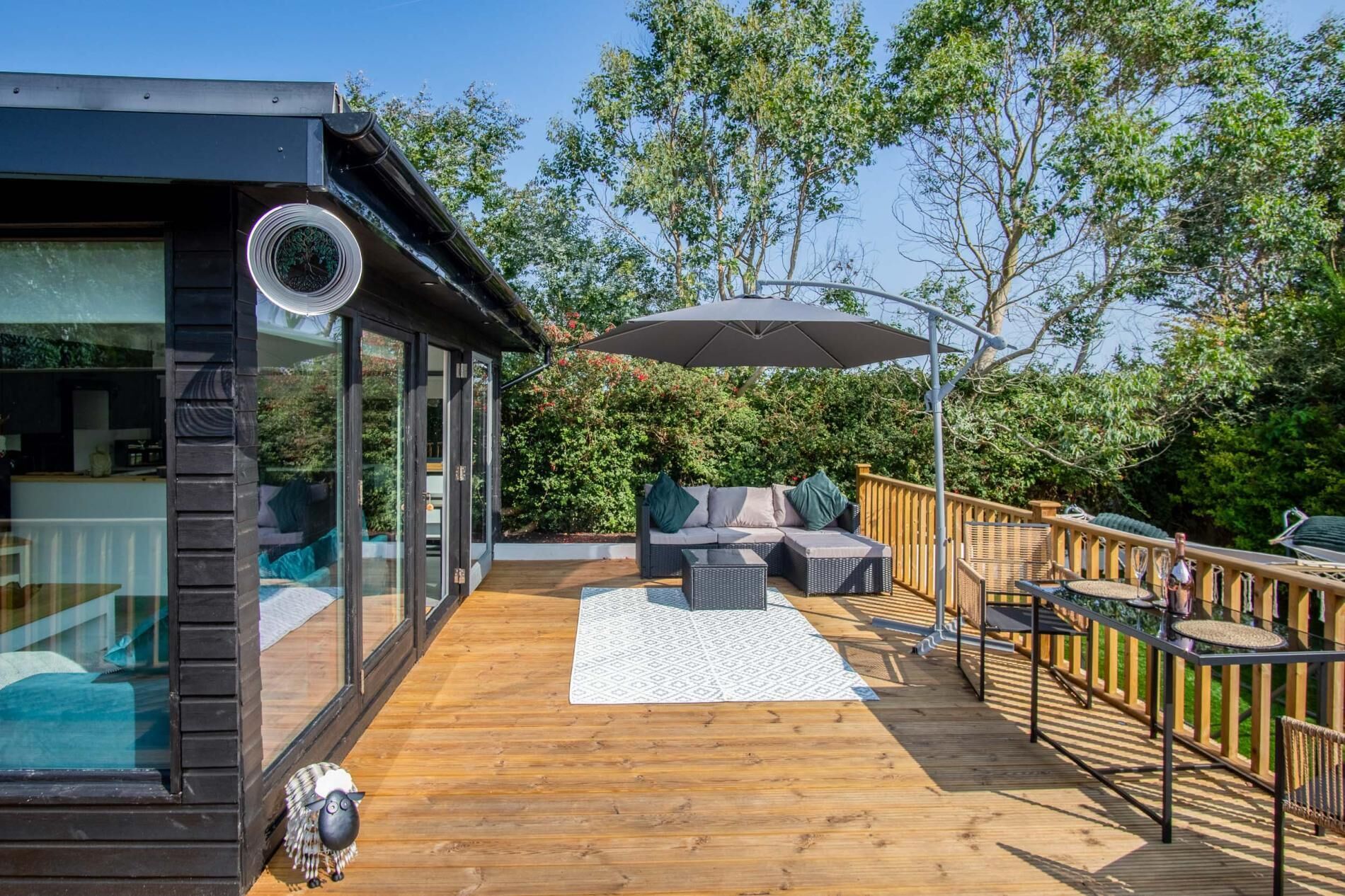 A wooden deck with outdoor furniture, a glass-enclosed room, and a large umbrella.