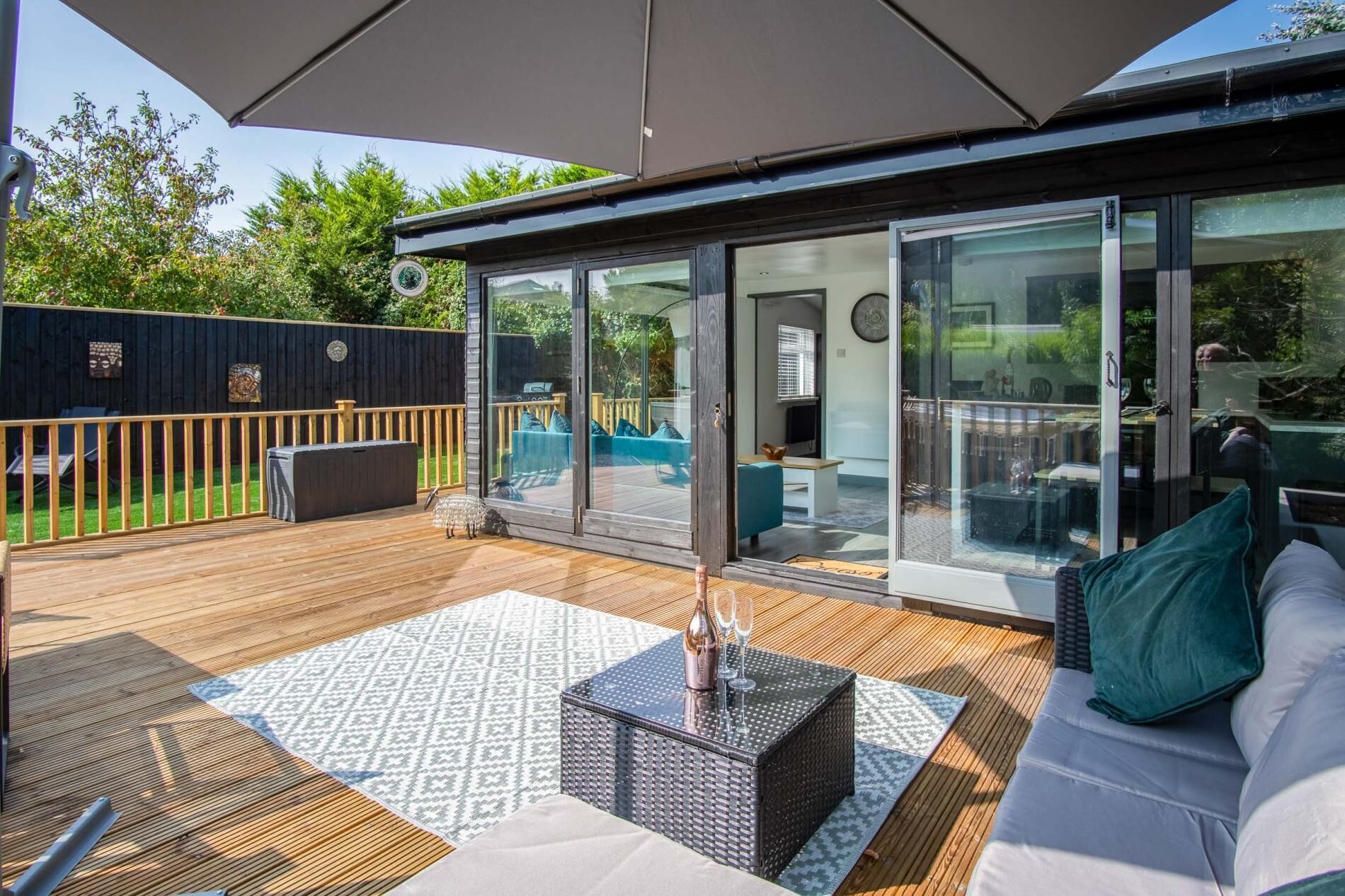 A deck with a glass door leading to a patio area, a sofa, a table, and a small outdoor kitchen.
